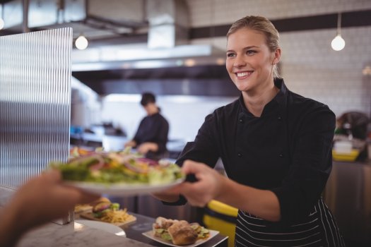 Foto af en smilende dame i en kantine, der serverer mad.