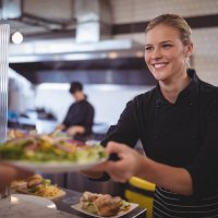 Foto af en smilende dame i en kantine, der serverer mad.