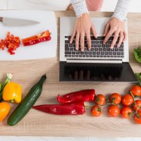 Illustrationsfoto af en person, der arbejder på en computer med grøntsager på et bord.